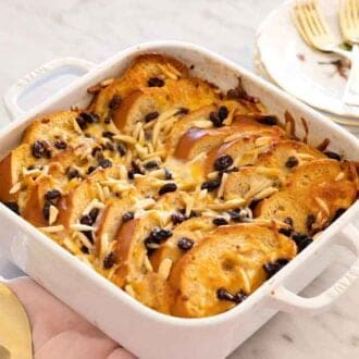 A baking dish with capirotada by a stack of plates and forks.
