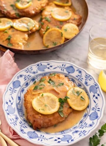 A plate of chicken Francese with a glass of wine in the background alongside a skillet.
