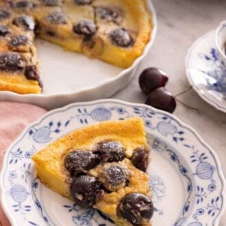 Pinterest graphic of a slice of clafoutis on a plate with powdered sugar dusted on top.