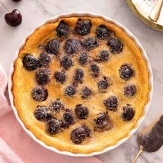 Overhead view of clafoutis in a baking dish by a linen and pie cutter.