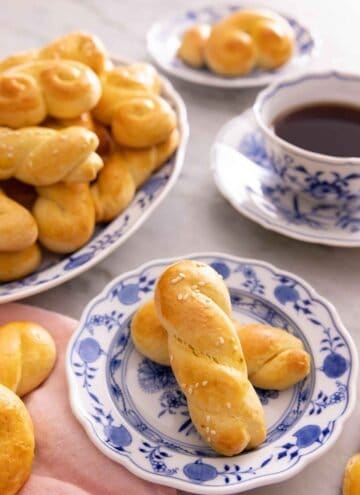 A plate with two koulourakia by a mug of coffee and a platter more.