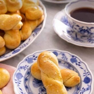 Pinterest graphic of a plate with two koulourakia by a platter more and a mug of coffee.