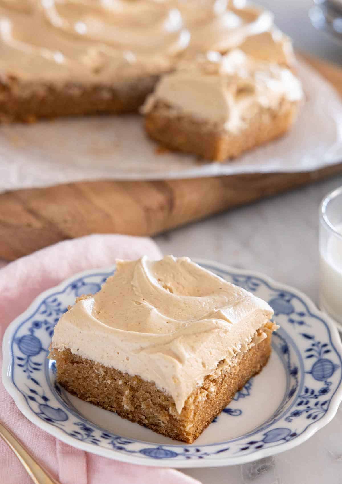 A square slice of peanut butter cake on a plate with the rest in the background.