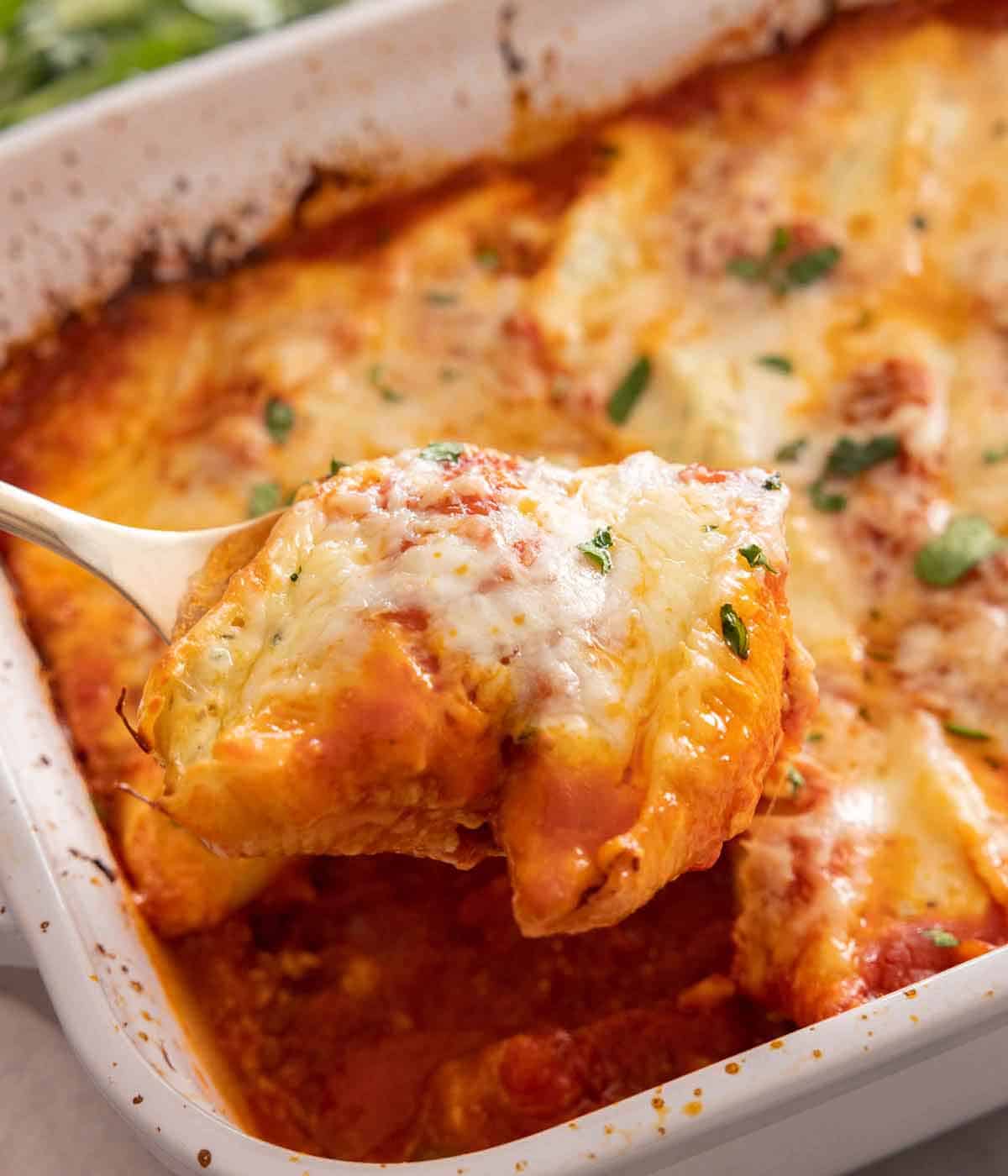 A baking dish with a spoonful of stuffed shells lifted from the dish.