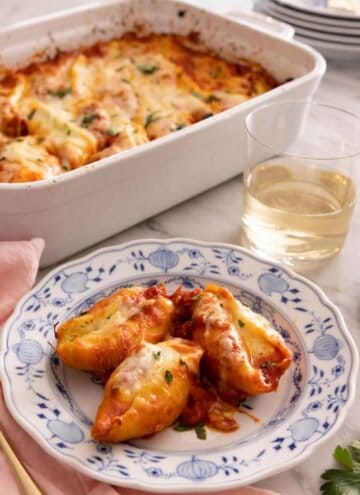 A plate with three stuffed shells by a glass of wine by a baking dish.