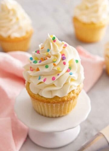 A mini cupcake stand with a vanilla cupcake on top with Swiss meringue buttercream and sprinkles.