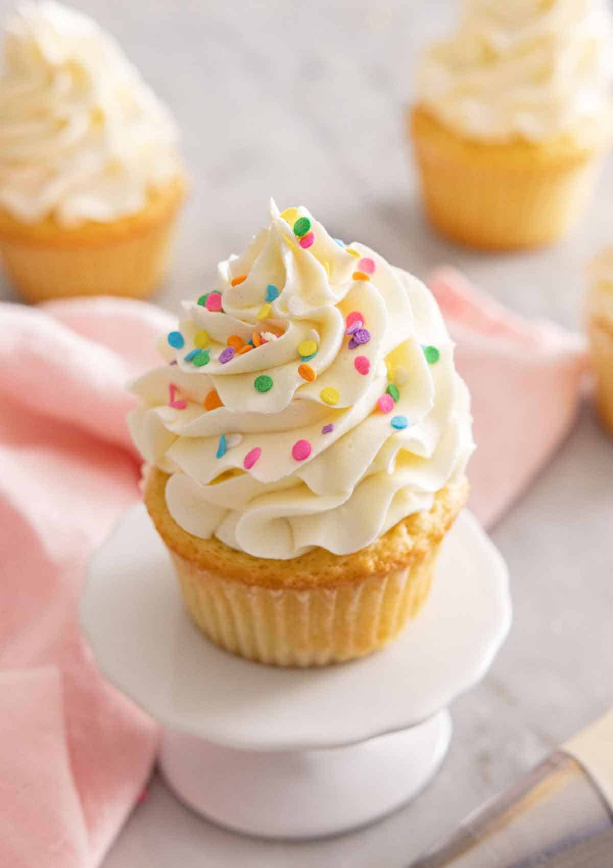 A mini cupcake stand with a vanilla cupcake on top with Swiss meringue buttercream and sprinkles.