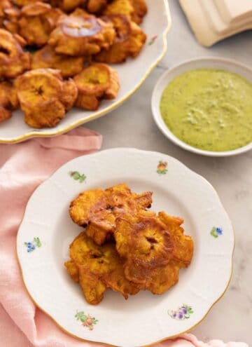 A plate with tostones with additional on a platter in the back along with dip.