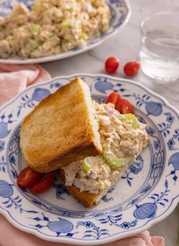 Tuna salad on toasted bread on a blue and white plate.