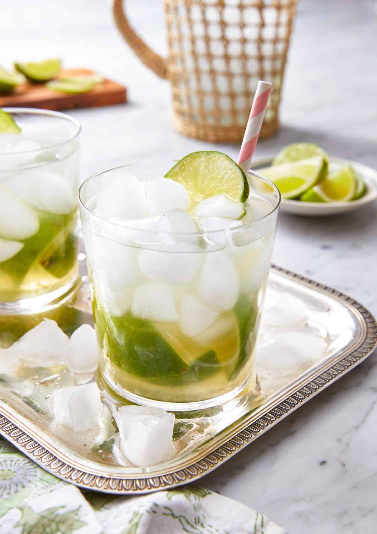 A silver tray with two glasses of caipirinha with fresh lime and a straw on top.