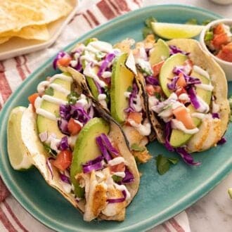 A platter of fish tacos with lime wedges and fresh cilantro around it.