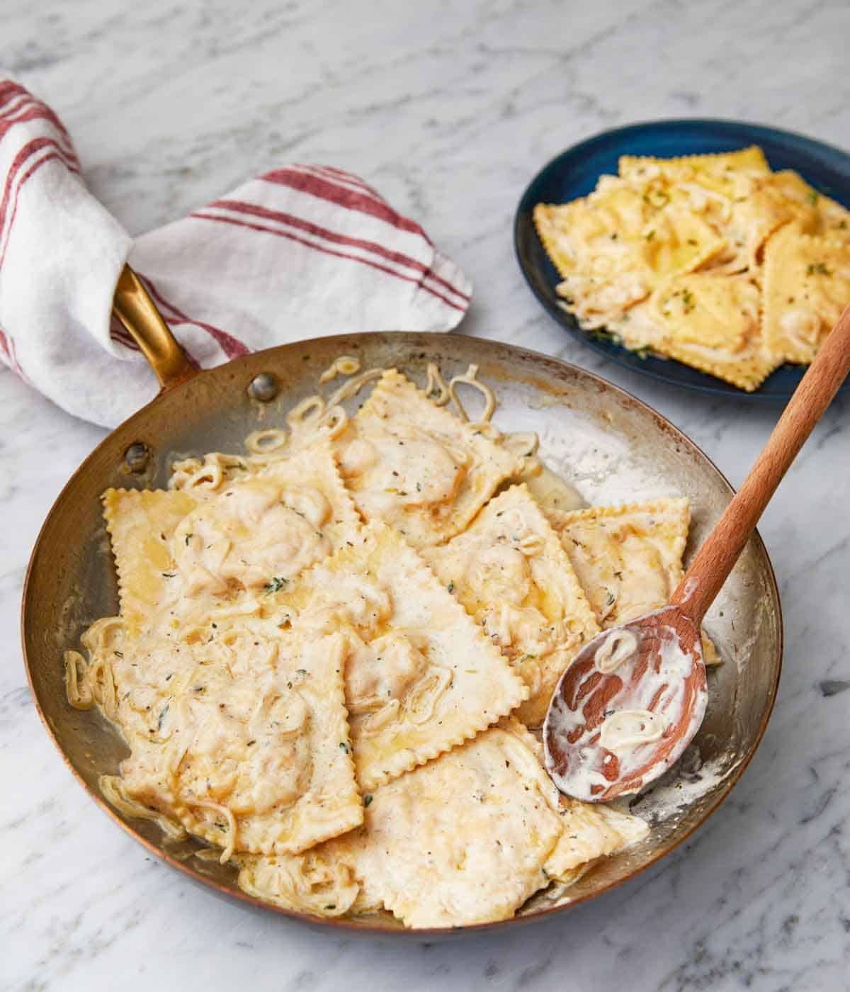 A skillet of lobster ravioli with a wooden spoon inside.