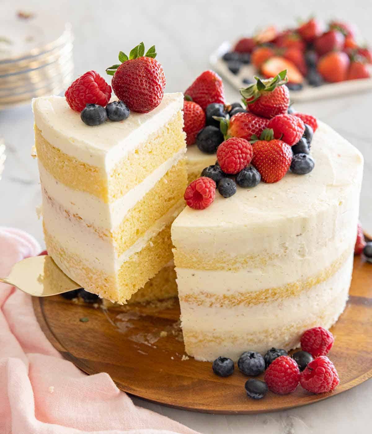 A naked cake with fresh berries on top with a slice being lifted out.