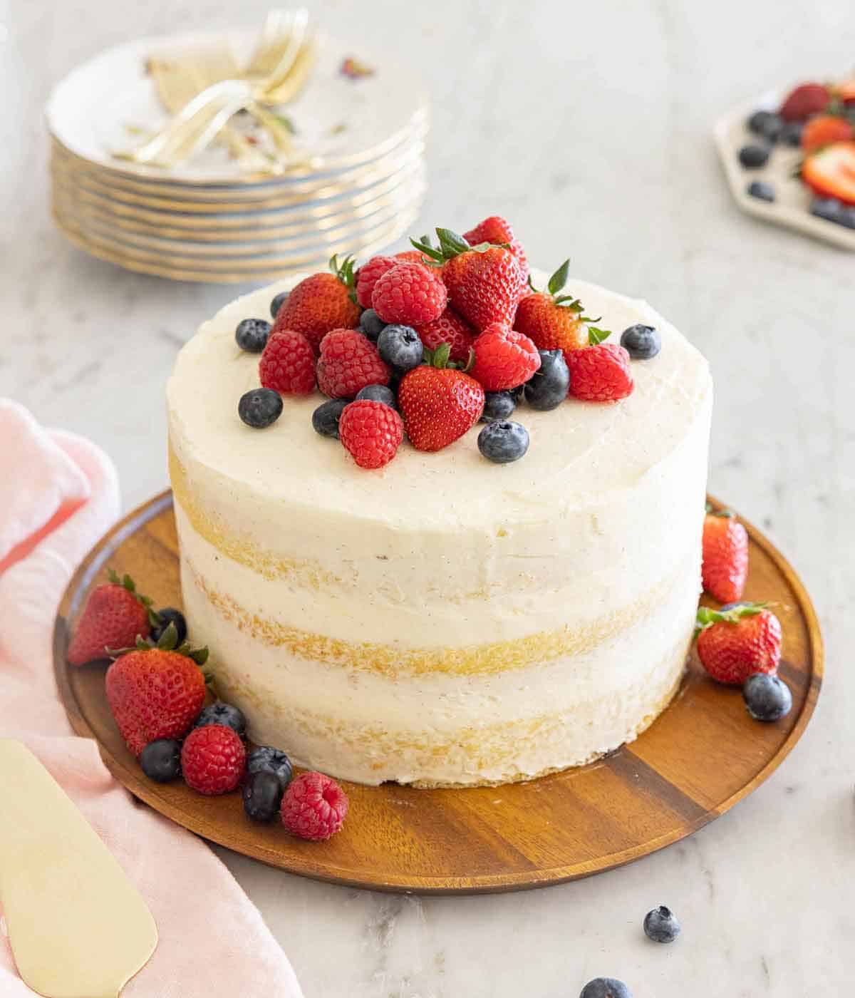 A naked cake with a pile of fresh berries on top and scattered at the base.