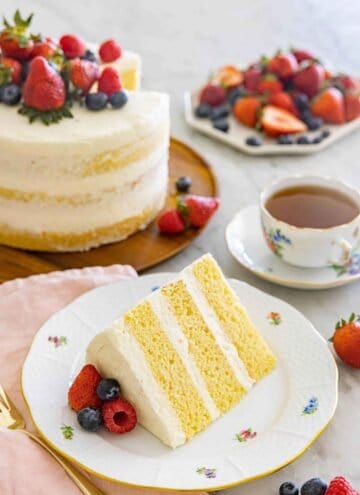 A plate with a slice of three layered naked cake by a mug of tea and the rest of the cake.