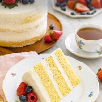 Pinterest graphic of a slice of naked cake on a plate with berries on top with the rest of the cake and a mug of tea behind it.