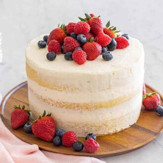 Fresh berries on top of a naked cake with a stack of plates in the background.