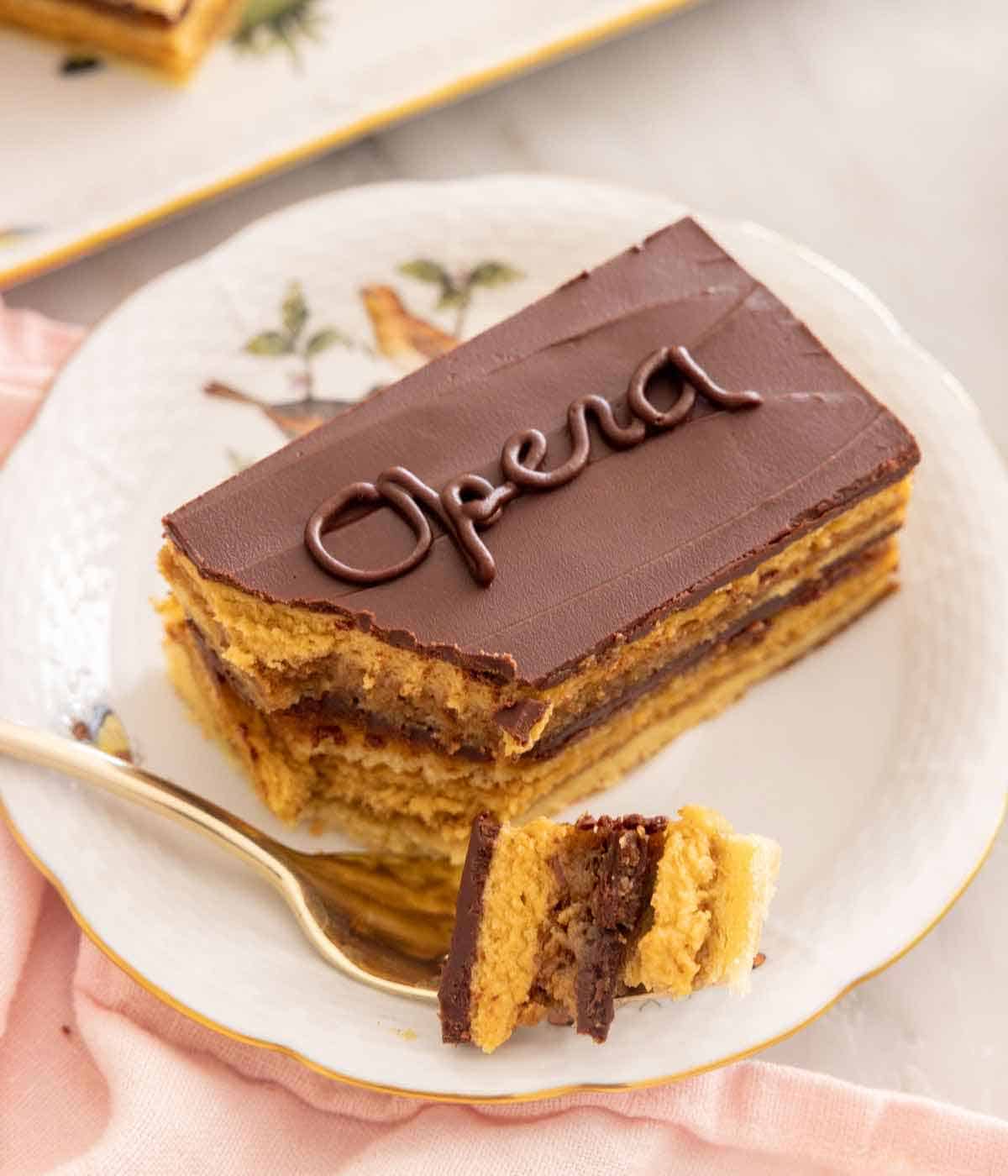 A plate with a piece of opera cake with a corner on a fork.