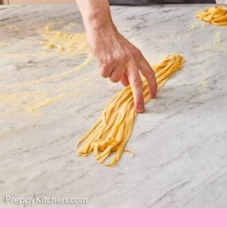 Pinterest graphic of a hand placing down a bunch of long strands of pasta dough.