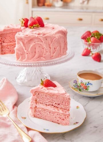 A strawberry cake on a cake stand with a slice cut and placed in front.