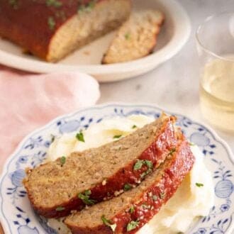 Pinterest graphic of a plate with two slices of turkey meatloaf on top of mashed potatoes with more meatloaf in the background.