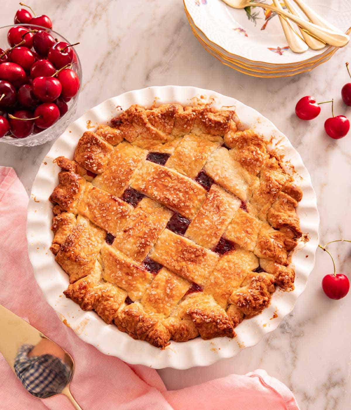 Overhead view of a cherry pie with fresh cherries in a bowl beside it and some scattered around.