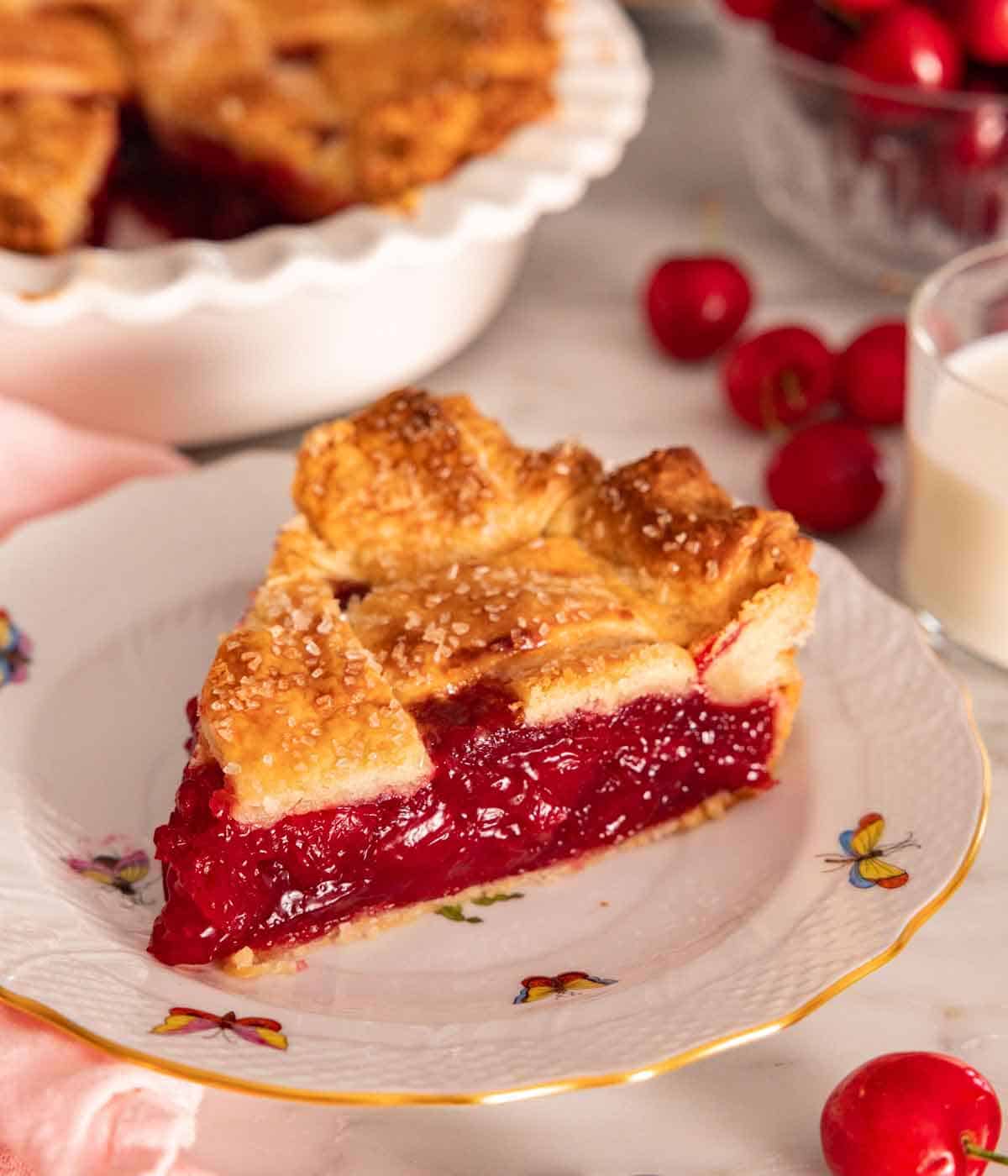 An angled photo of a slice of cherry pie on a plate, showing the red cherry filling.
