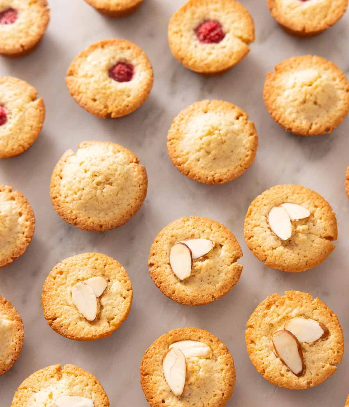 Overhead view of rows of financiers, some with raspberries and sliced almond toppings.