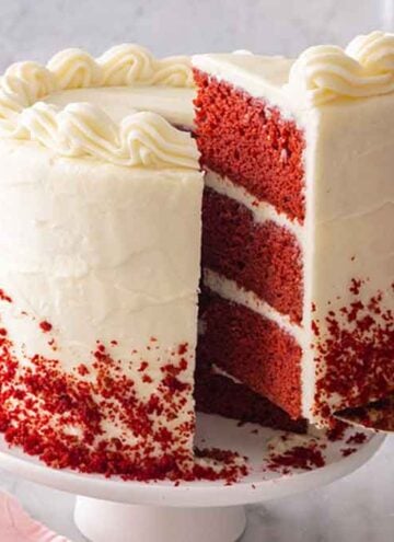 A slice of red velvet cake being lifted from the cake with a stack of plates in the background.