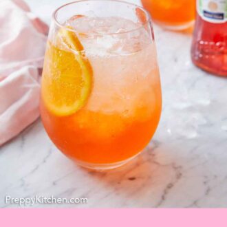 Pinterest graphic of a glass of aperol spritz with a slice of orange inside with more sliced oranges in the background.