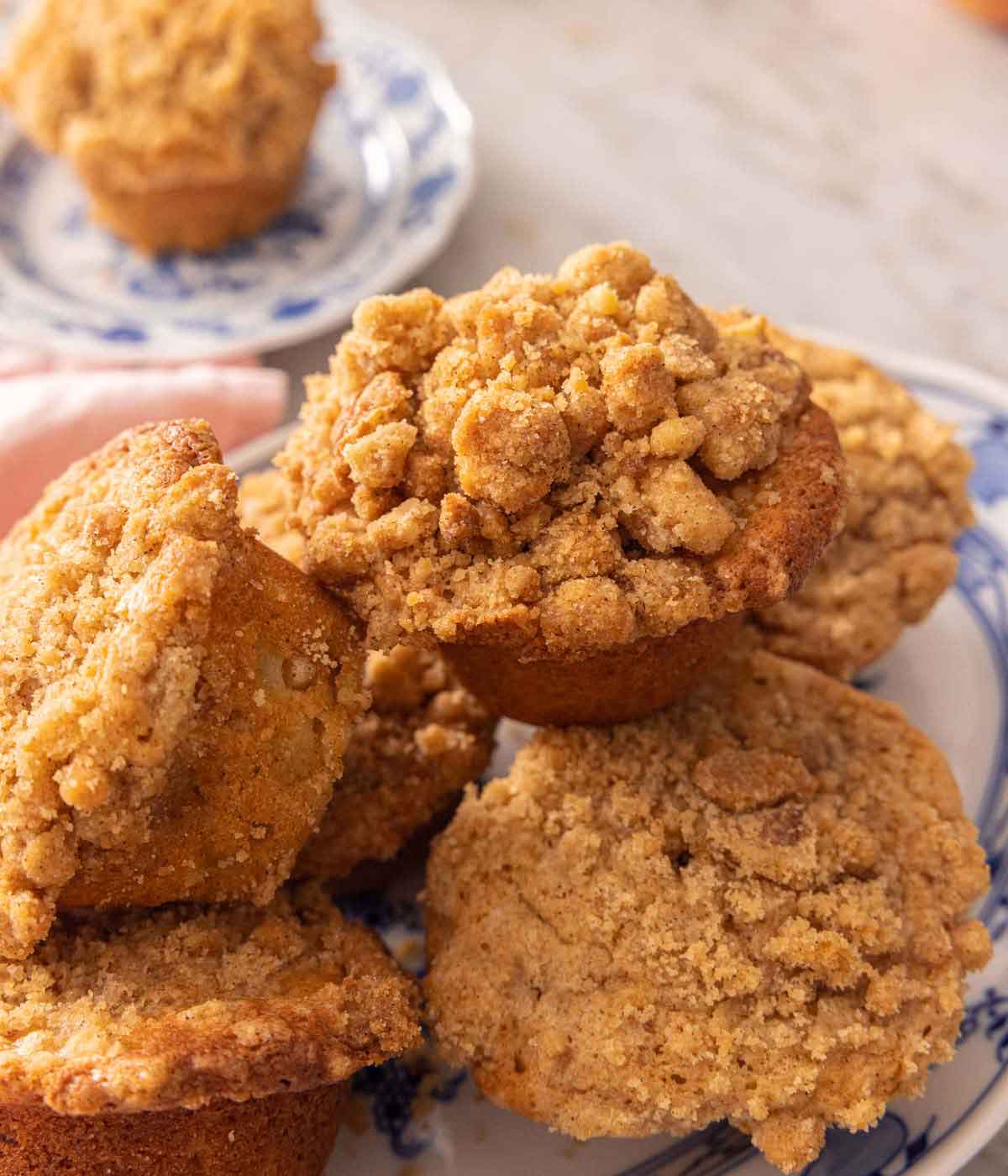 A platter with apple muffins in a pile with one on a plate in the background.