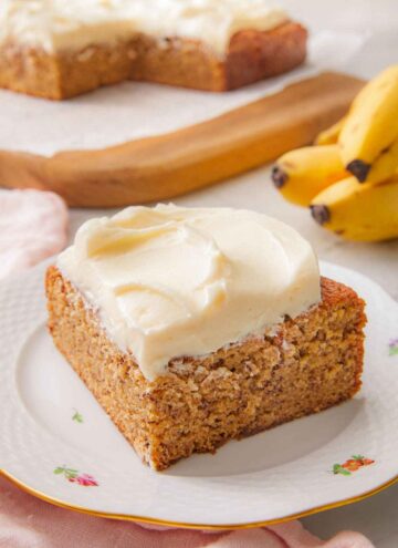 A slice of banana cake with a layer of cream cheese frosting spread on top on a small plate.