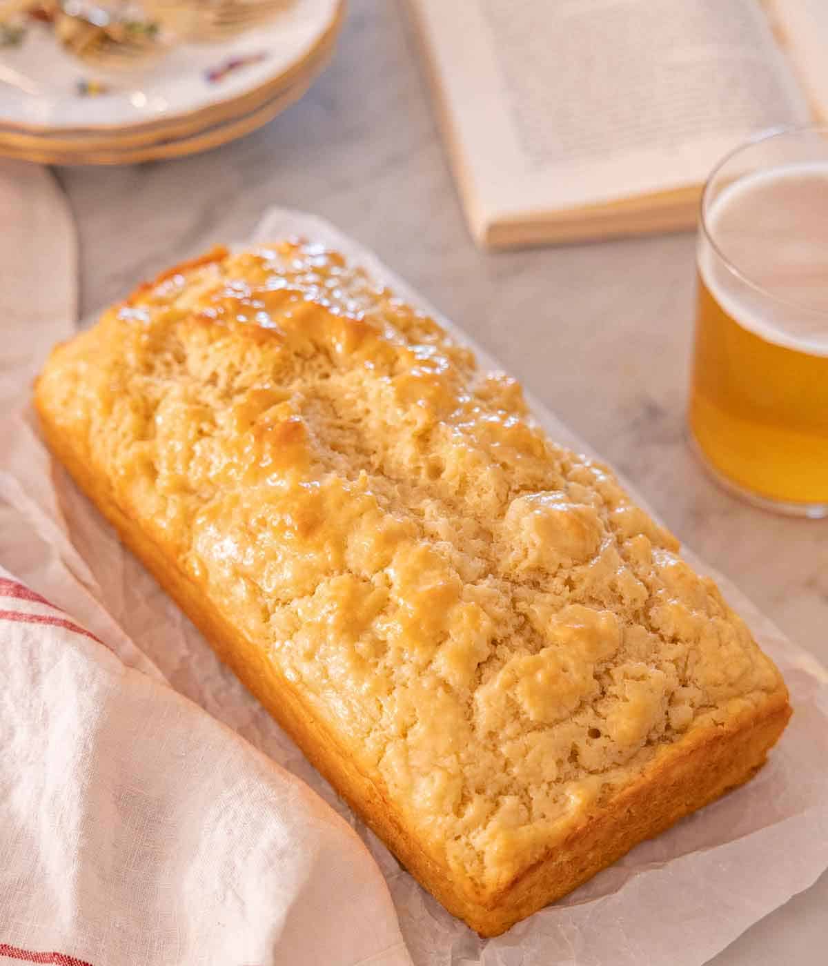 A loaf of beer bread with a drink on the side and a book in the back.