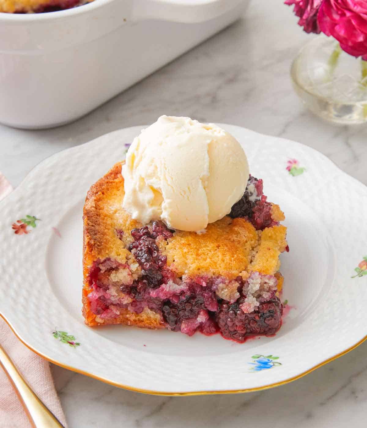 A plate with a square piece of blackberry cobbler with a scoop of vanilla ice cream on top.