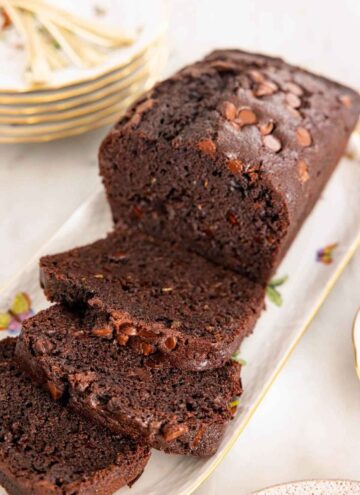 A platter with a loaf of chocolate zucchini bread with three slices cut in front.