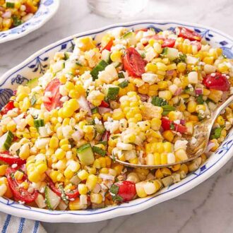 A large platter of corn salad with a serving spoon tucked in.