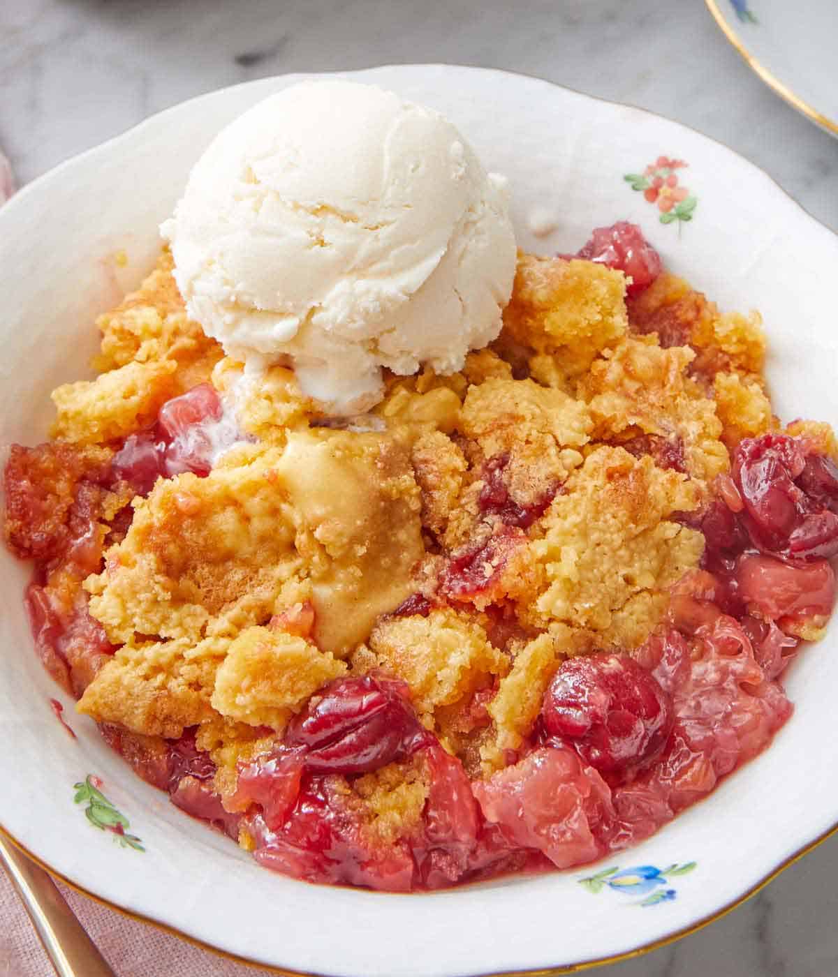 Close up of a bowl of a serving of dump cake with a scoop of vanilla ice cream.