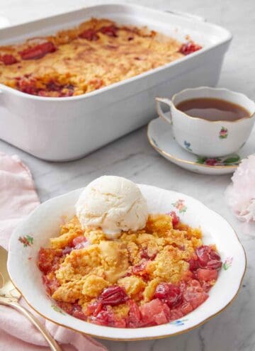 A plate with a serving of dump cake in a bowl with a scoop of ice cream and the baking dish and coffee in the background.