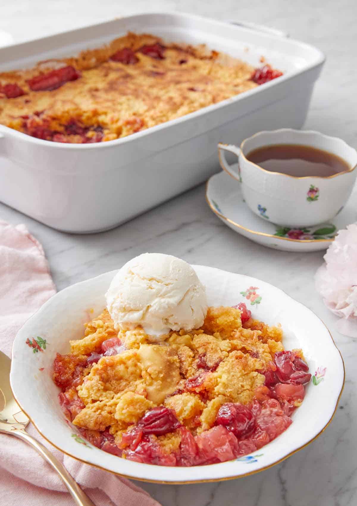 A plate with a serving of dump cake in a bowl with a scoop of ice cream and the baking dish and coffee in the background.