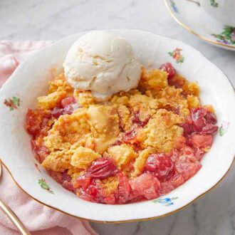 A bowl with dump cake and a scoop of vanilla ice cream and a spoon beside it.