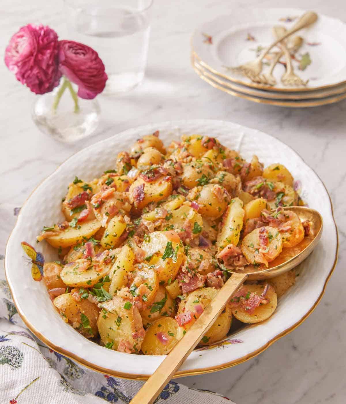 A serving platter of German potato salad with a serving spoon tucked in.
