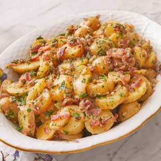 An oval platter of German potato salad with a serving spoon on the side.