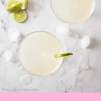 Pinterest graphic of an overhead view of two glasses of gimlet with cut lime and ice scattered around.