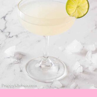 Pinterest graphic of a glass of gimlet with a slice of lime on the rim with ice scattered on the counter.