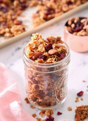 A mason jar filled with granola with a sheet pan with granola in the background, out of focus.