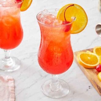 Two glasses of the cocktail hurricane drink with garnish in the drink and on a wooden cutting board.