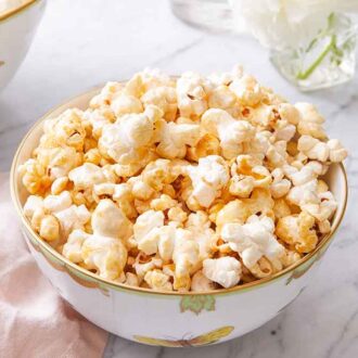 A bowl of kettle corn with a glass of water beside it and popcorn scattered on the counter.