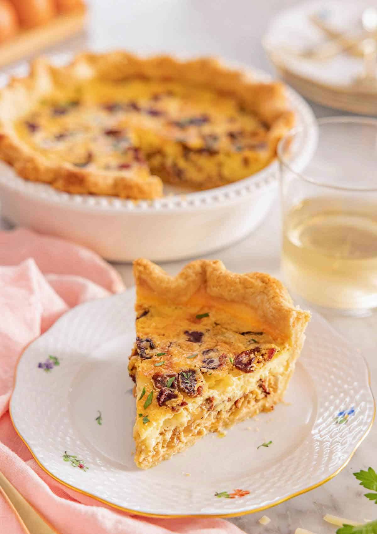 A plate with a slice of quiche Lorraine with the rest of the quiche in the background.