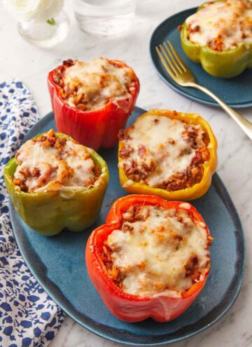 A platter with four stuffed peppers with a plate with a single one in the background.