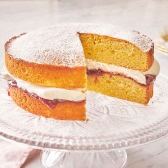 A cake stand with a Victoria sponge cake on top with a slice cut out.